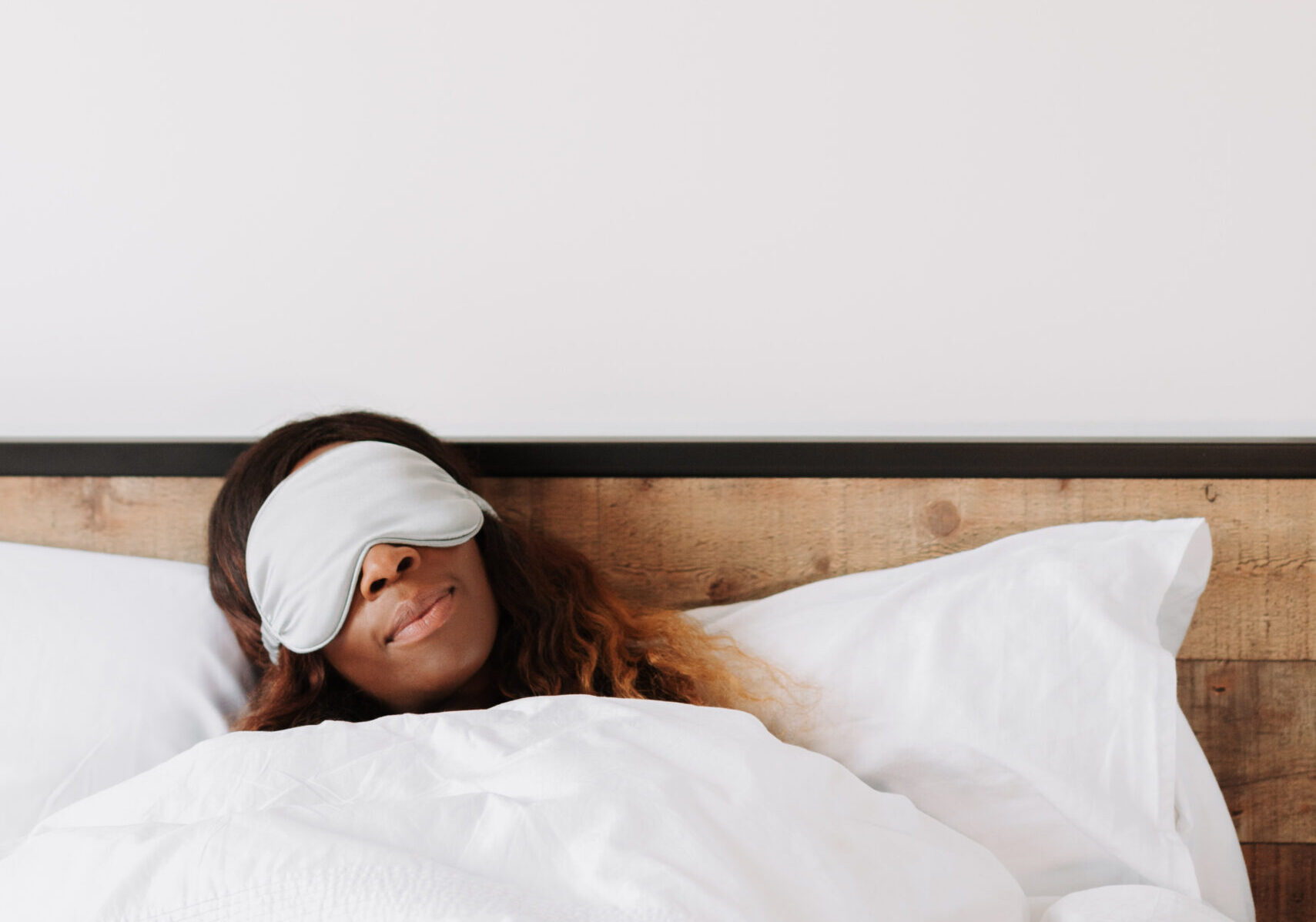 Black woman sleeping in bed wearing a silk sleep mask